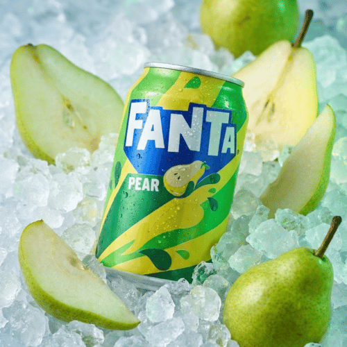 Eine gelb-grüne Dose Fanta Pear steht zentral in einem Bett aus zerstoßenem Eis. Umgeben ist die Dose von frisch aufgeschnittenen, saftigen Birnenscheiben und ganzen grünen Birnen. Das Design der Dose zeigt eine stilisierte Birnen-Illustration auf grünem Grund.